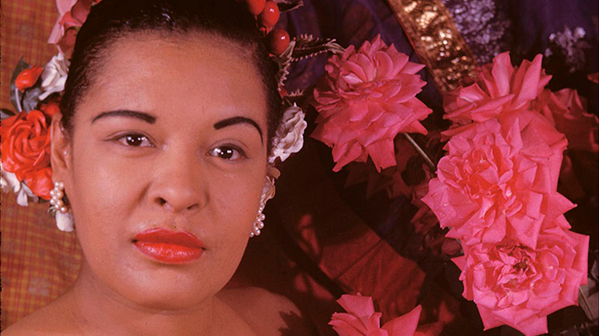 Kasvokuva laulajatar Billie Holidaysta kukkien ympäröimänä.