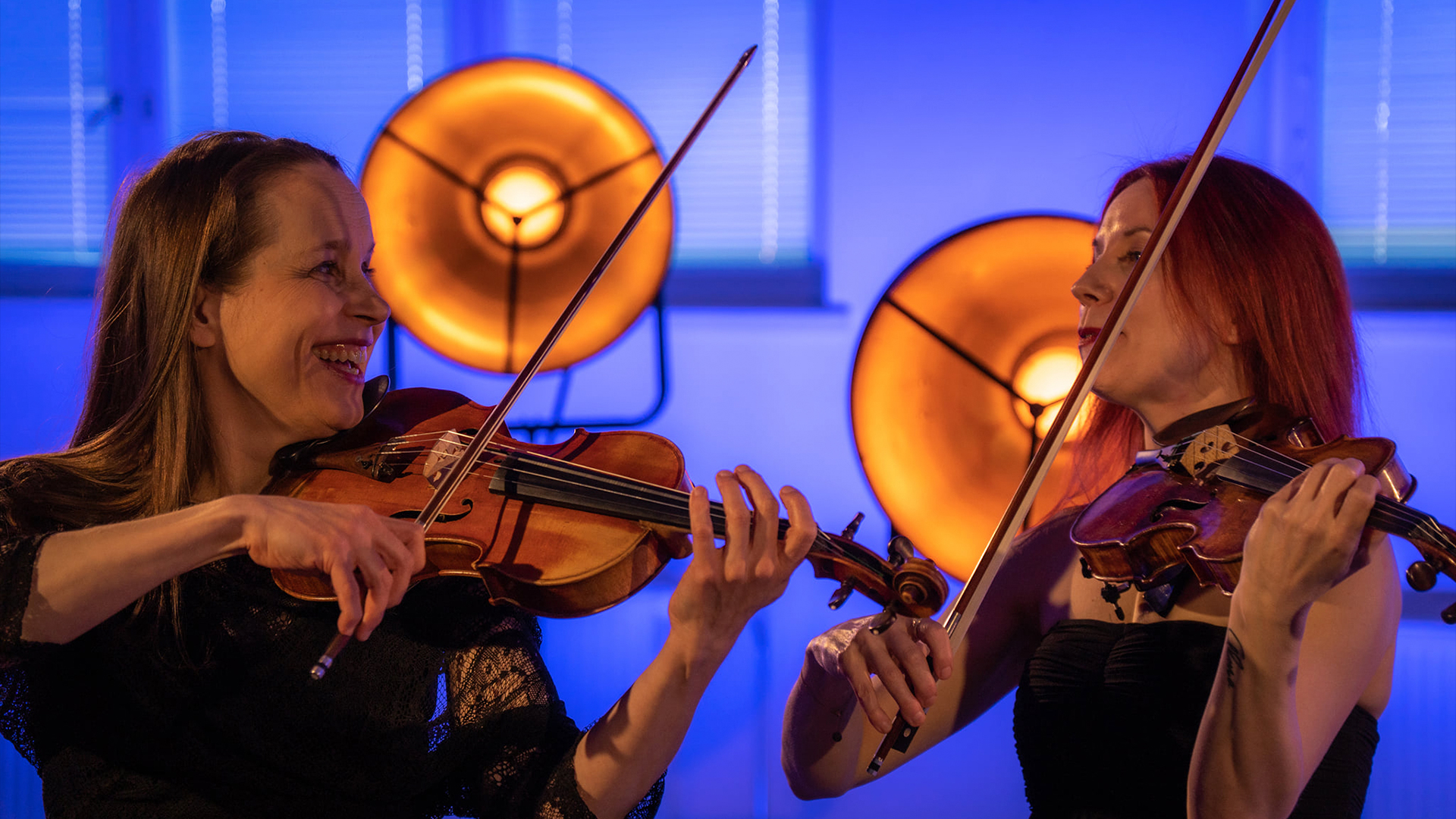 Muusikot Rista Tuura ja Elina Kivistö soittamassa viulua hymyillen.