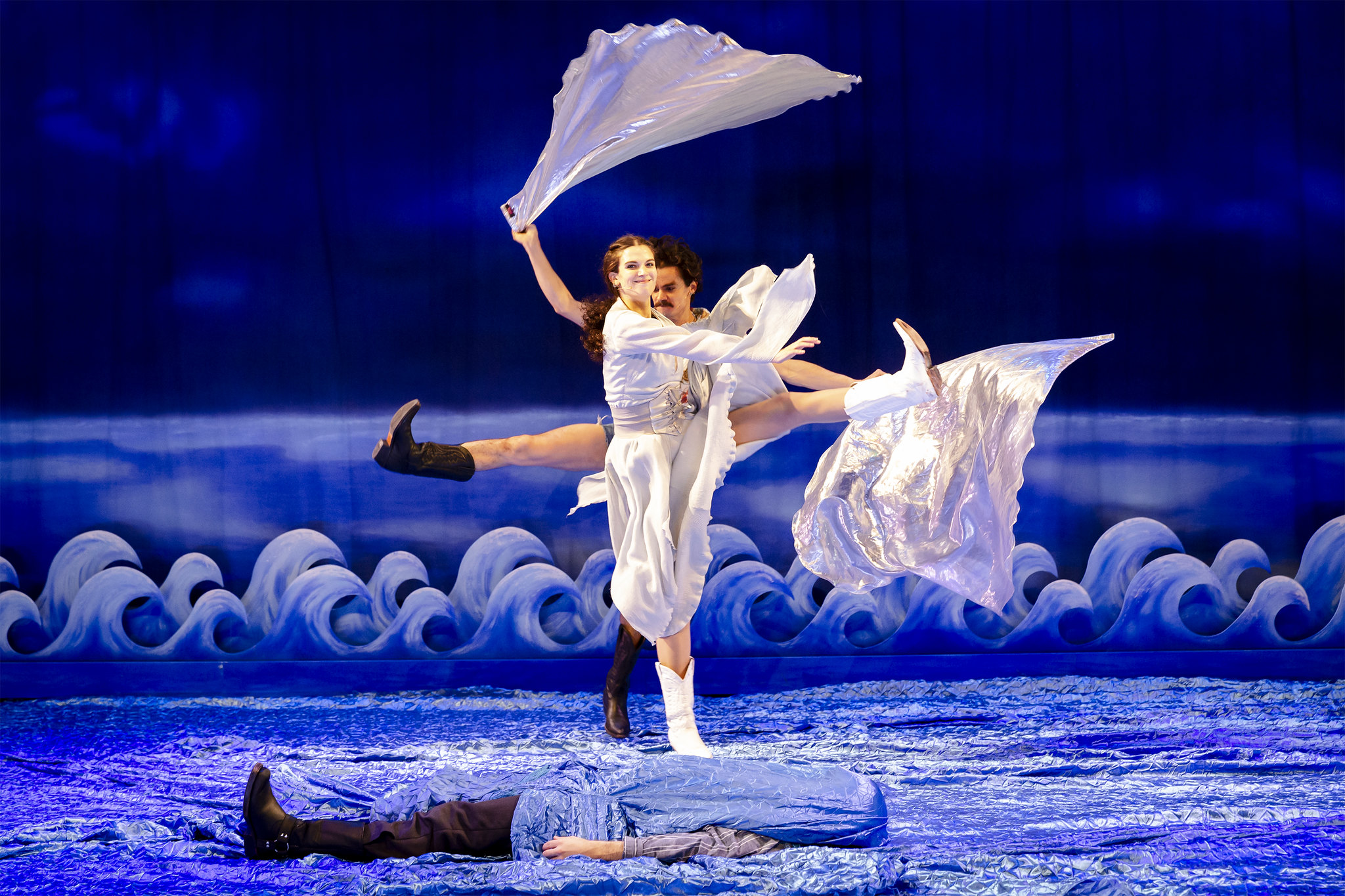 Kaksi tanssijaa seisovat vaativassa asennossa keskellä sinisiä lavasteita.