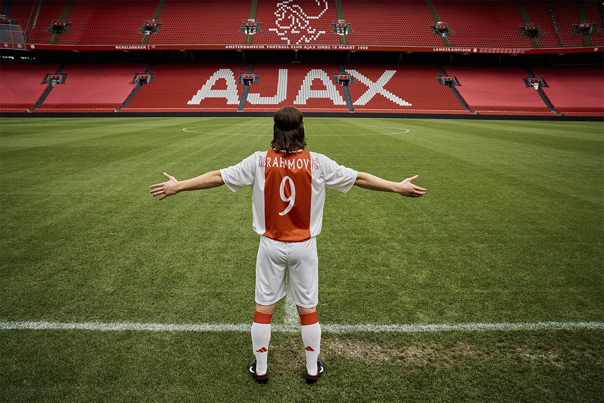 Zlatan står på en tom fotbollsplan. Ajax logo syns i bakgrunden.